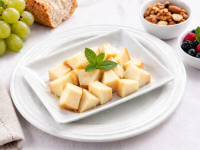 Plato de dados de queso semi-curado decorado con menta, acompañado de uvas, frutos secos y frutos rojos.