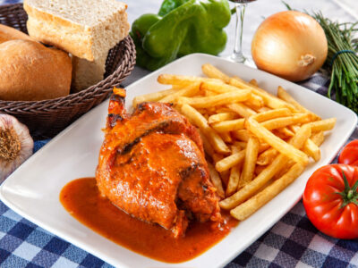 Bandeja blanca con pieza de codillo asado salseado, patatas fritas crujientes y guarnición rústica.