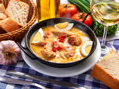 Cazuela de guiso tradicional de boda con albóndigas, trozos de carne y huevo cocido sobre plato y mantel de cuadros.