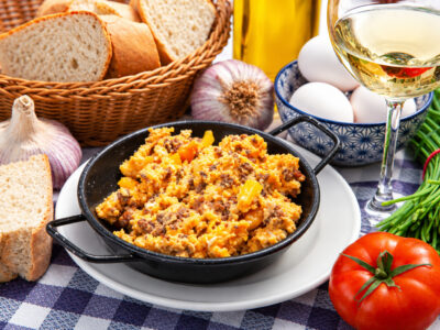 Cazuela de revuelto de huevos a la porreta sobre plato y mantel de cuadros, acompañado de pan, vino y bodegón manchego.