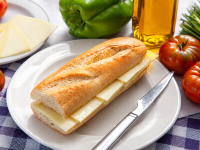 Montado de queso manchego curado en pan de barra sobre un plato blanco.