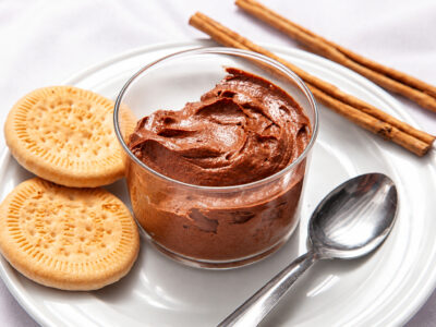 Vaso transparente con mousse cremosa de chocolate sobre plato blanco con galletas y cuchara.