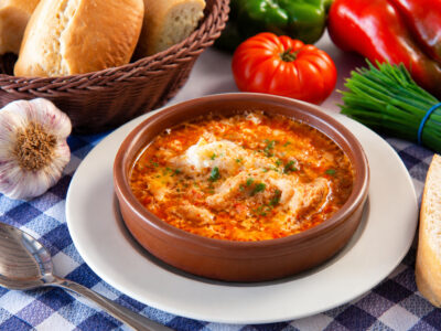 Cazuela de barro con sopa de ajo castellana tradicional con huevo y pimentón sobre plato y mantel de cuadros.
